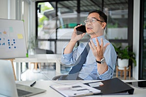 Experienced senior businessman having a serious phone call with his employee while sitting in the office room