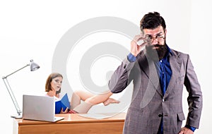 Experienced and skilled. Executive coach fixing his glasses while sexy woman working in background. Business coach with