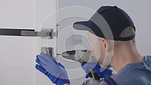 An experienced worker adjusts the door closing mechanism. A locksmith installs a handle and a lock on interior doors.