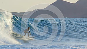 Experienced young male surfer carves over a large crashing wave on a sunny day.