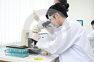 An expert Asian male scientist examining a virus specimen under a microscope in the lab