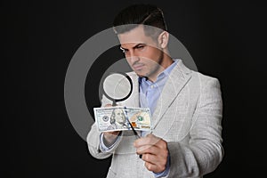 Expert authenticating 100 dollar banknote with magnifying glass against black background. Fake money concept