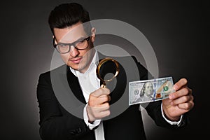 Expert authenticating 100 dollar banknote with magnifying glass against dark background. Fake money concept
