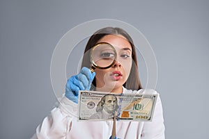 Expert authenticating 100 dollar banknote with magnifying glass on light grey background. Fake money concept