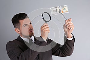 Expert authenticating 100 dollar banknote with magnifying glass on light grey background. Fake money concept