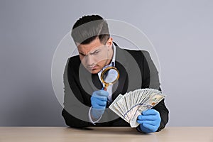 Expert authenticating 100 dollar with magnifying glass at table on light grey background. Fake money concept