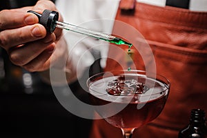 Expert barman is making cocktail finishing up by dropping green bitter