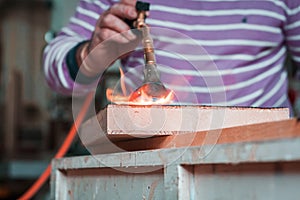 Expert carpenter burning a wood slab with a professional gas burner. Flames and smoke, fire and timber.