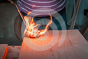 Expert carpenter burning a wood slab with a professional gas burner. Flames and smoke, fire and timber.