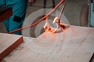 Expert carpenter burning a wood slab with a professional gas burner. Flames and smoke, fire and timber.