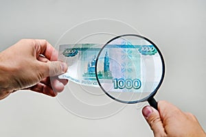 Expert with magnifying glass checks suspicious money