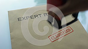 Expert review classified, hand stamping seal on folder with important documents