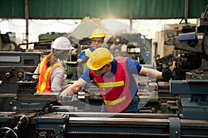 An expert technician is inspecting industrial machinery in a steel factory. Engineers are working and repairing machines in