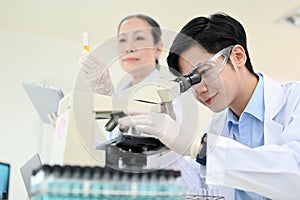 An expert young Asian male scientist examining a virus specimen under a microscope