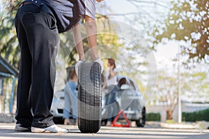 Expertise mechanic man in uniform holding a tire for help a woman for changing car wheel on the highway, car service, repair,