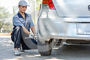 Expertise mechanic man  in uniform using force trying to unscrew the wheel bolts nuts and help a woman for changing car wheel on