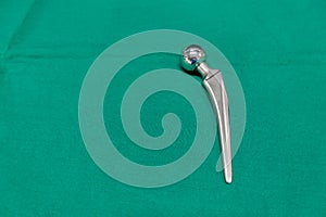 explanted femoral prosthesis lies on a green surgical drape