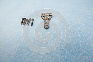 explanted titanium plate and 4 titanium screws for the treatment of a radius fracture are lying on a light blue support