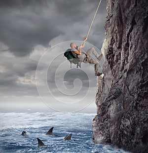 Explorer climbs a mountain with the risk to fall on the sea with sharks
