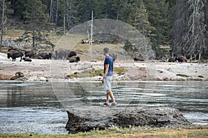 Explorer looking at bison while standing by lake in famous Yellowstone park