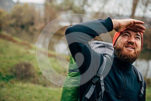 Explorer young man hiking in mountains with travel backpack looking to a beautiful view with hand on the forehead.