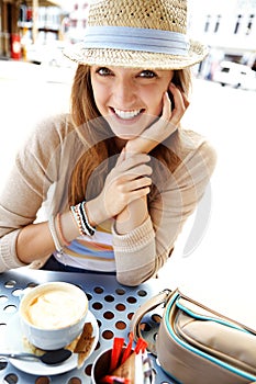 Exploring the city one coffee shop at a time. A happy young woman smiling at the camera while sitting at a sidewalk