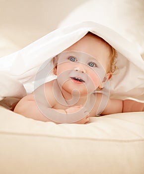 Exploring his world. Cute baby boy lying under a sheet playfully and looking away.