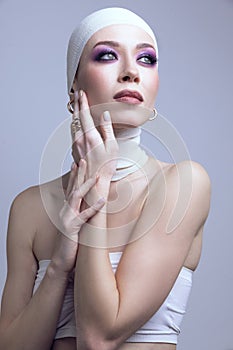 Exploring modern beauty trends. young woman, with purple eyeshadow makeup, hand on cheek, posing on pastel purple