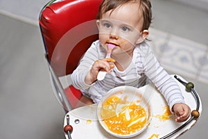 Exploring new tastes. A cute little baby sitting in a highchair eating solid food.