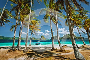 Exploring Palawan most famous touristic spots. Palm trees and lonely island hopping tour boat on Ipil beach of tropical