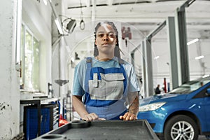 Exploring repairing. African american woman, professional female mechanic pulling, carrying tool box cart in auto repair