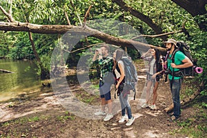 Exploring, researches and expedition concept. Four tourists are hiking near the river in a wild spring wood, guy is looking in the