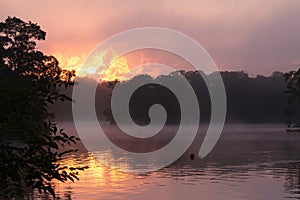 Explosive dawn sunrise over a calm, misty lake