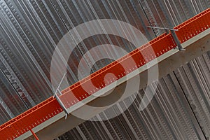 Exposed corrugated metal decking system with orange wire trunking underneath a concrete floor