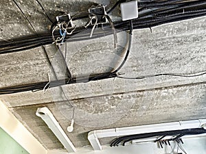 Exposed electrical wiring and conduits along a gray concrete ceiling in an industrial setting photo