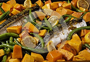 Exposition of healthy and tasty makerel with vegetbles on plate and black table. pumpkin, beans, lemon and makerel.