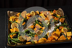 Exposition of healthy and tasty makerel with vegetbles on plate and black table. pumpkin, beans, lemon and makerel.