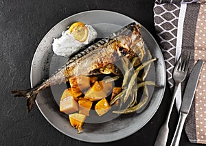 Exposition of healthy and tasty makerel with vegetbles on plate and black table. pumpkin, beans, lemon and makerel.