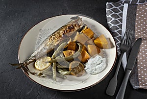 Exposition of healthy and tasty makerel with vegetbles on plate and black table. pumpkin, beans, lemon and makerel.