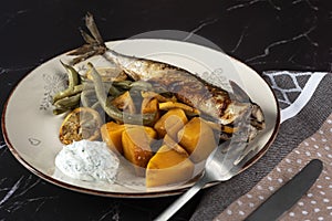 Exposition of healthy and tasty makerel with vegetbles on plate and black table. pumpkin, beans, lemon and makerel.