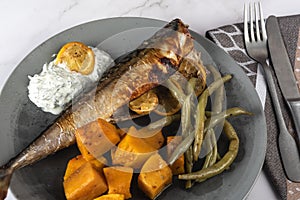 Exposition of healthy and tasty makerel with vegetbles on plate and black table. pumpkin, beans, lemon and makerel.