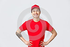 Express delivery, shipping and logistics concept. Smiling charismatic asian male delivery man in red cap, t-shirt, hold