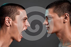 Expressing rage. Close up of two young angry caucasian twin brothers arguing, shouting while standing face to face