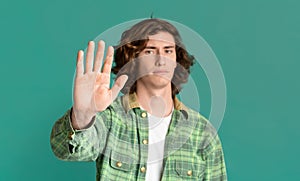 Expressing rejection. Serious millennial guy showing STOP gesture on color background