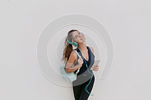 Expressing true positive emotions of joyful young woman in sportswear enjoying lovely music in headphones on white photo