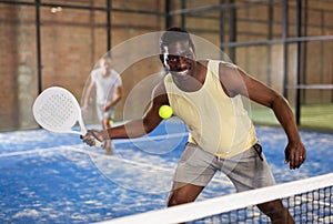 Expressive african american playing paddle ball on closed court