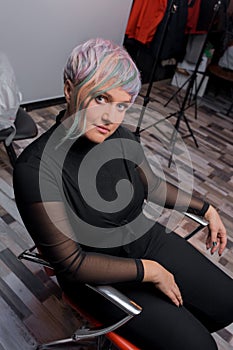 Expressive beautiful adult Caucasian woman with make-up looking at the camera sitting in a salon chair with a stylish, fashionable