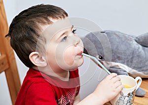 expressive boy drinking orange juice through a plastic straw