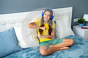 Expressive emotional excited teen girl. Teenager girl in headphones relax on bed at home using headphones, singing and