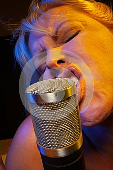 Expressive female vocalist under gelled lighting sings with passion into condenser microphone